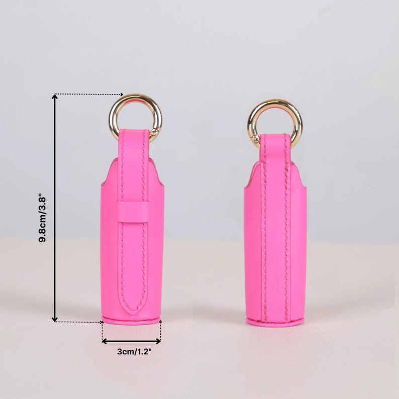 May include: Two bright pink lipstick cases with gold-tone metal rings at the top. The cases feature a vertical strap design and measure 3.8 inches in height and 1.2 inches in width as indicated by the visible measurement lines and text.