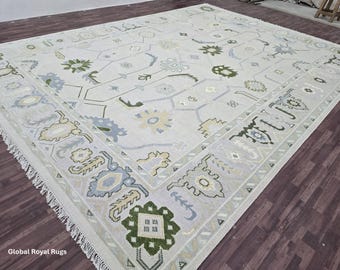 May include: Large, rectangular area rug with a light gray background and a detailed floral pattern in shades of green, blue, and yellow. The rug has a fringe border and is placed on a dark wood floor. The text "Global Royal Rugs" is visible.