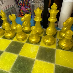 Pu&ograve; includere: Un set di scacchi giallo con pezzi disposti su una scacchiera gialla e verde. I pezzi sono realizzati in un materiale lucido e traslucido.