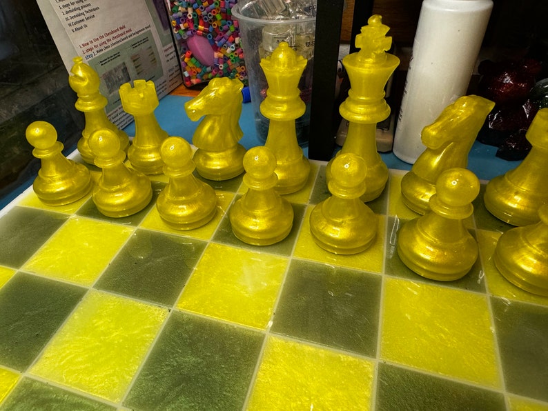 Pu&ograve; includere: Un set di scacchi giallo con pezzi disposti su una scacchiera gialla e verde. I pezzi sono realizzati in un materiale lucido e traslucido.