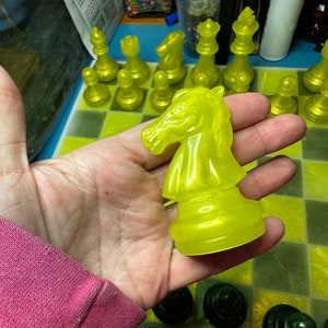 Pu&ograve; includere: Un pezzo di cavaliere degli scacchi giallo con una finitura lucida e traslucida. Il pezzo &egrave; tenuto in una mano, con una scacchiera sullo sfondo.