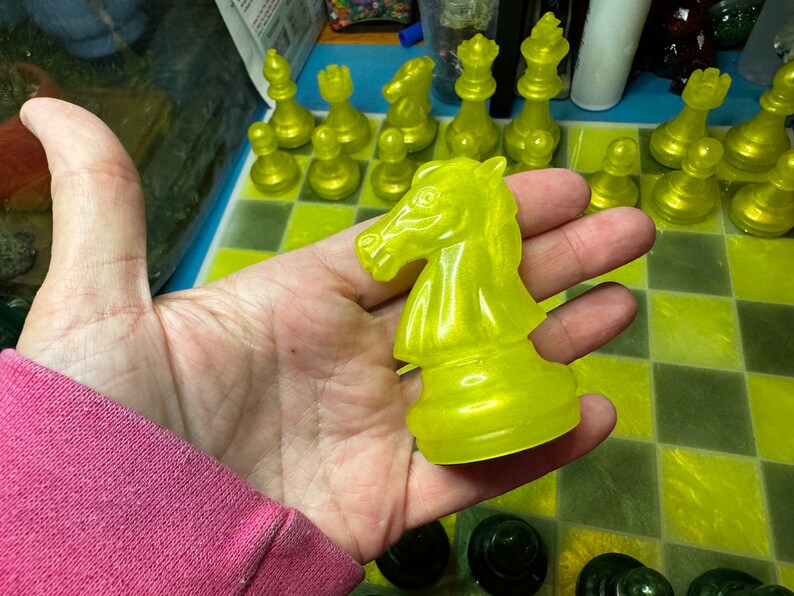 Pu&ograve; includere: Un pezzo di cavaliere degli scacchi giallo con una finitura lucida e traslucida. Il pezzo &egrave; tenuto in una mano, con una scacchiera sullo sfondo.