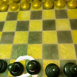 Pu&ograve; includere: Una scacchiera verde e gialla con pezzi degli scacchi verdi sulla fila inferiore. I pezzi degli scacchi sono fatti di un materiale lucido.