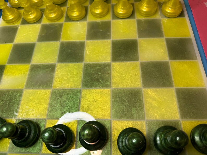 Pu&ograve; includere: Una scacchiera verde e gialla con pezzi degli scacchi verdi sulla fila inferiore. I pezzi degli scacchi sono fatti di un materiale lucido.