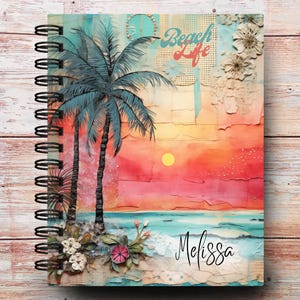 May include: Spiral-bound notebook with a beach-themed cover. The cover features a vibrant sunset scene with palm trees, ocean, and the words "Beach Life." The name "Melissa" is written in cursive. The notebook has a wooden background.