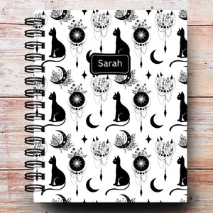 May include: A white spiral bound notebook with a black and white pattern of cats, moons, and stars. The notebook has a personalized name tag that says "Sarah".
