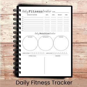 May include: A spiral-bound fitness tracker notebook with a black cover. The white interior pages include sections for workout routines, nutrition, water intake, and sleep hours. The text "Daily Fitness Tracker" is at the bottom.