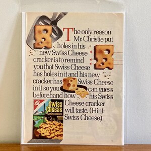May include: A vintage advertisement for Swiss Cheese crackers. The text reads: "The only reason Mr. Christie put holes in his new Swiss Cheese cracker is to remind you that Swiss Cheese has holes in it and his new cracker has Swiss Cheese in it so you can guess beforehand how his Swiss Cheese cracker will taste. (Hint: Swiss Cheese)"