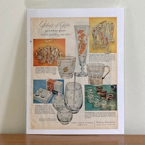 May include: A vintage advertisement for Galaxy of Gifts, featuring a variety of glassware, including a tall glass, a pitcher, and a set of tumblers. The ad features a gold and white design with the text "Galaxy of Gifts" and "Each a sparkling new star!"
