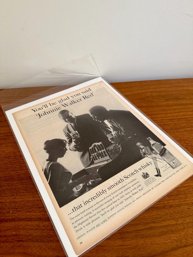 May include: Vintage advertisement for Johnnie Walker Red Scotch whisky. The black and white image features people enjoying the drink. Text includes "You'll be glad you said Johnnie Walker Red" and details about the whisky.