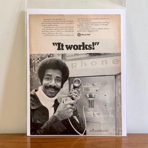 Peut inclure: Une photo en noir et blanc d'un homme utilisant un téléphone public. L'homme sourit et tient le combiné du téléphone à son oreille. La légende dit "Ça marche !" et est une publicité vintage pour Illinois Bell.