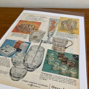 May include: A vintage advertisement for Libbey Safedge glassware featuring a set of gold-rimmed glasses with a Grecian key design. The ad text reads "Gifts in Libbey glass, each a sparkling new idea!" and "Continental Cups. A 22K gold Grecian Key design bands each sparkling glass and is repeated in the handsome golden holder-made detachable for easy wash-ups. Beautiful-yet practical-and the stunningly gift-boxed set of 8 is only about $7.50".