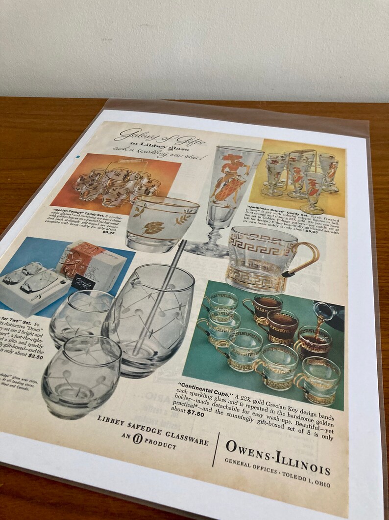 May include: A vintage advertisement for Libbey Safedge glassware featuring a set of gold-rimmed glasses with a Grecian key design. The ad text reads "Gifts in Libbey glass, each a sparkling new idea!" and "Continental Cups. A 22K gold Grecian Key design bands each sparkling glass and is repeated in the handsome golden holder-made detachable for easy wash-ups. Beautiful-yet practical-and the stunningly gift-boxed set of 8 is only about $7.50".