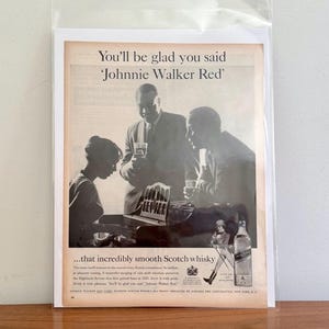 May include: Vintage advertisement for Johnnie Walker Red Scotch whisky. The black and white image features three people, one playing a piano, and two others holding glasses. Text reads "You'll be glad you said 'Johnnie Walker Red'" and "...that incredibly smooth Scotch whisky."