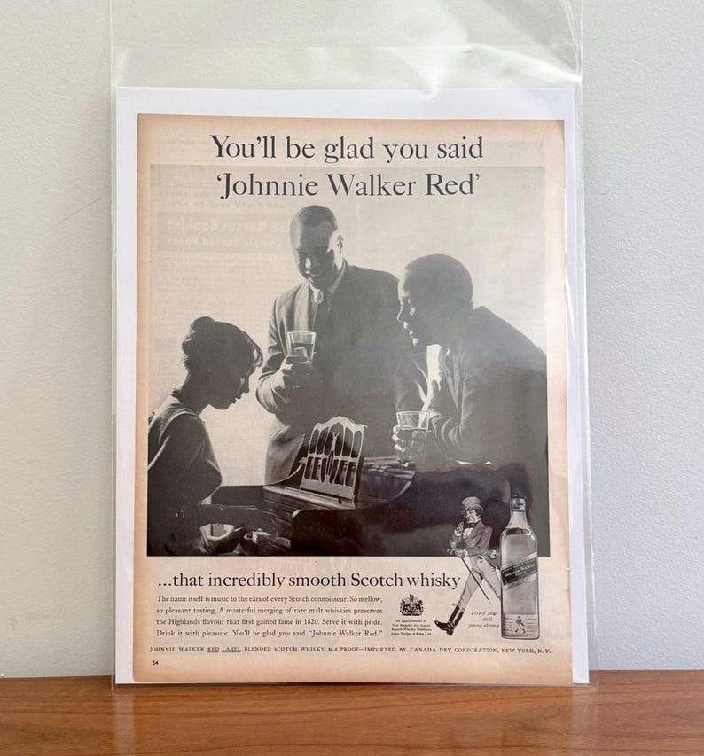 May include: Vintage advertisement for Johnnie Walker Red Scotch whisky. The black and white image features three people, one playing a piano, and two others holding glasses. Text reads "You'll be glad you said 'Johnnie Walker Red'" and "...that incredibly smooth Scotch whisky."