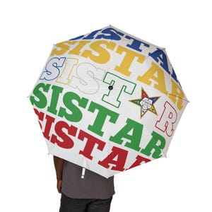 May include: White umbrella with the word "SISTER STAR" in red, green, yellow, and blue block letters. The umbrella also features a star emblem with a red, green, and white star design.