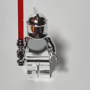 May include: A silver chrome Lego minifigure with a red lightsaber. The minifigure is wearing a silver chrome helmet with a black visor.