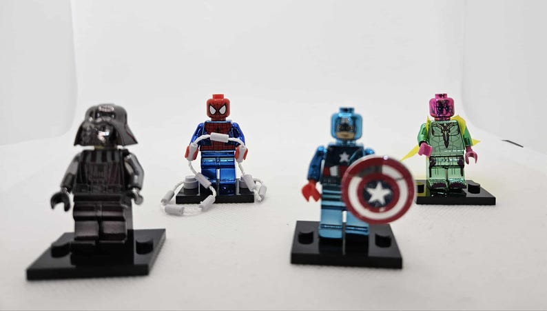 May include: Four superhero-themed Lego minifigures on black bases. Includes Darth Vader in black, Spider-Man in red and blue with web accessories, Captain America with shield, and Vision in green and pink.