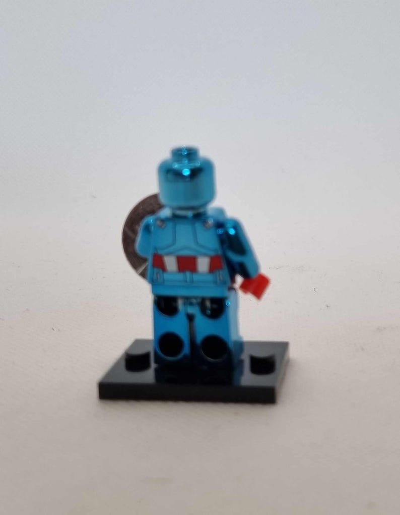 May include: A metallic blue Lego minifigure of a superhero, with red and white accents on the torso and red gloves. The figure is standing on a black base and holding a silver disc. The overall theme is collectibles.