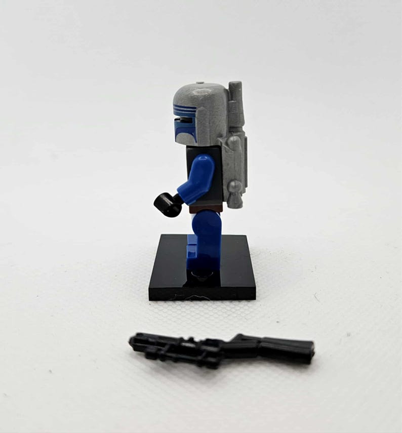 May include: A Lego minifigure of a character in a gray helmet with blue accents, blue arms and legs, and a gray backpack. The figure stands on a black base, with a black blaster rifle in front.