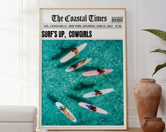 May include: A framed poster featuring a newspaper-style design with the headline "SURF'S UP, COWGIRLS." The image within shows surfers on colorful surfboards in turquoise water. The poster is displayed in a room with a white ottoman and decorative vases.