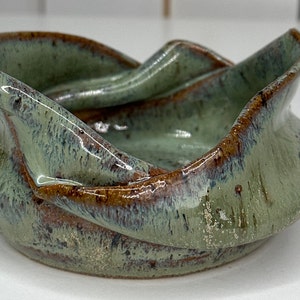 May include: A small, green and brown ceramic bowl with a unique, wavy design. The bowl has a glossy finish and a slightly textured surface.