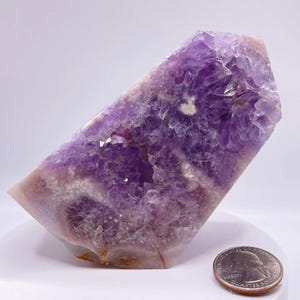 May include: A large amethyst geode with a purple and white crystal formation. The geode is about the size of a US quarter.