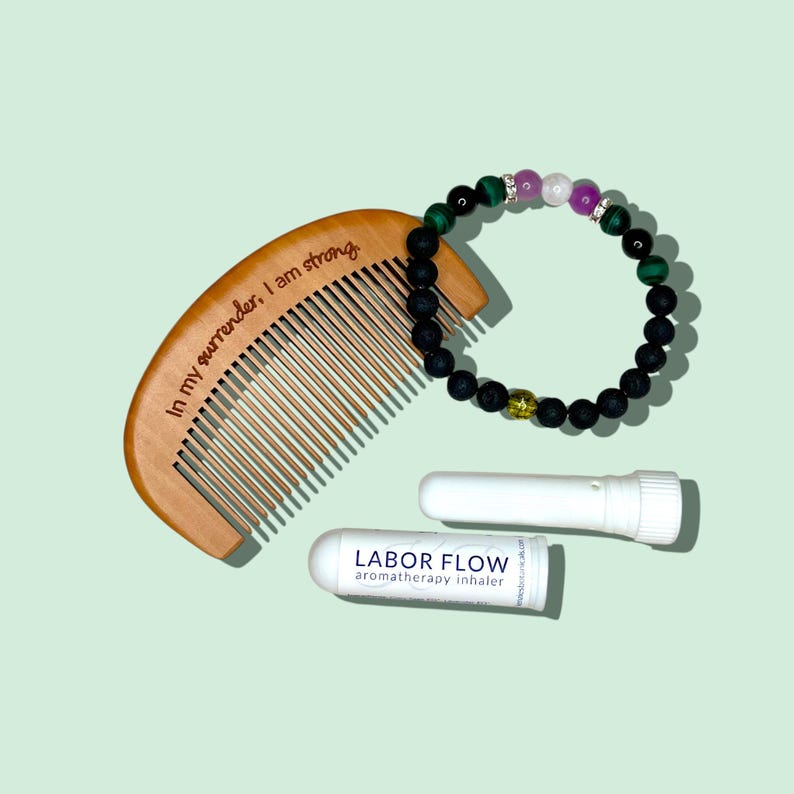 May include: A wooden comb with the text "In my surrender, I am strong" is next to a beaded bracelet with green, purple, and white stones. Two white aromatherapy inhalers are also present. The products are on a light green background.