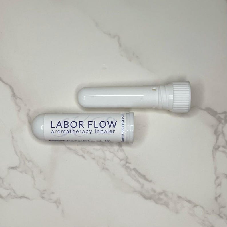 May include: Two white aromatherapy inhalers, one assembled and one disassembled, are displayed on a marble surface. The assembled inhaler has the text "LABOR FLOW aromatherapy inhaler" printed on it. The disassembled inhaler has a screw-on cap.