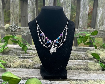 May include: A silver necklace with a fairy charm, featuring a layered chain with purple and blue iridescent beads and star accents.