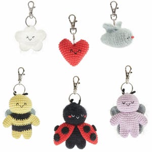 May include: A collection of six crochet keychains in various shapes and colors. The keychains include a white cloud, a red heart, a blue whale, a yellow and black bee, a black ladybug, and a lavender butterfly. Each keychain has a silver clasp.