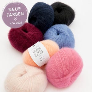 Op de afbeelding: Zeven bollen pluizig garen in diverse kleuren, waaronder crème, perzik, roze, blauw, donkerblauw, zwart en bordeauxrood. Eén perzikkleurige bol heeft een wit label met Luxury Merino Alpaca Dream, 50 g - 125 m. Een paarse cirkel toont NEUE FARBEN H/W 2026.