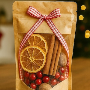 May include: A kraft paper bag with a clear window, filled with dried orange slices, cinnamon sticks, cranberries, and nutmeg. A red and white checkered ribbon is tied in a bow around the bag, suggesting a festive theme.