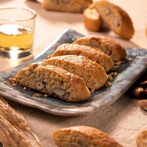 Può includere: Primo piano di un piatto di biscotti biscotti con mandorle. I biscotti sono dorati e hanno una consistenza croccante. Il piatto è blu e bianco con un design rustico. Ci sono anche alcune mandorle sparse intorno al piatto.