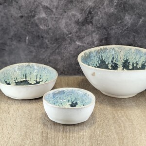 Può includere: Tre ciotole in ceramica bianca con una glassa blu e bianca. Le ciotole sono annidate l'una dentro l'altra, con la ciotola più grande in basso e la più piccola in alto.