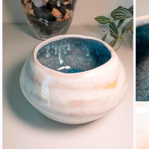Può includere: Una ciotola in ceramica bianca con una glassa blu all'interno. La ciotola ha una forma arrotondata e un esterno testurizzato.