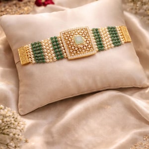 Peut inclure: Un bracelet doré avec une pièce centrale carrée ornée de rangées alternées de perles et de perles vertes. La pièce carrée comporte une pierre vert clair et est entourée de petites pierres transparentes. Le bracelet repose sur un coussin crème.