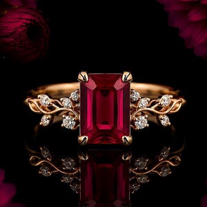 May include: A rose gold ring featuring a large, rectangular, emerald-cut deep red gemstone at the center. The band is designed with delicate, vine-like metalwork adorned with small, round, clear white stones on both sides of the central gem.
