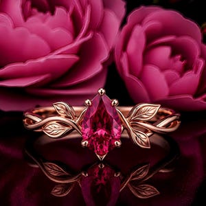 Può includere: Un anello in oro rosa con una pietra preziosa rosa brillante taglio a pera al centro. La fascia presenta dettagli intricati di foglie metalliche e motivi a viticcio che si estendono dalla montatura, creando un aspetto botanico lucido.