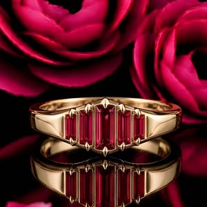 May include: A gold ring featuring five vertically set, rectangular baguette-cut red gemstones arranged in a graduated fan-like pattern. The metal band is polished and smooth, with small pointed prongs securing each of the vibrant red stones.