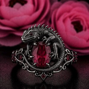 Puede incluir: Un anillo de metal oscuro con una figura de lagarto texturizada enroscada alrededor de una piedra preciosa roja profunda de corte ovalado. La banda muestra intrincados patrones de volutas y pequeñas piedras rojas en los laterales.