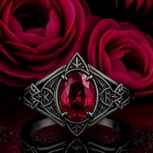 May include: A dark gunmetal ring featuring an oval-cut deep red gemstone set in a prong setting. The band displays intricate metalwork with geometric patterns and etched runic symbols on both sides of the central stone, creating a pointed frame.