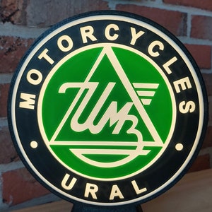 May include: A black and green round sign with the words "Motorcycles Ural" and a white stylised logo of a triangle with the letters "UM" inside.