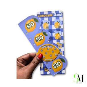 Puede incluir: Un conjunto de seguimiento de ahorros con temática Lemonade Stand que incluye una tarjeta a cuadros azules y blancos con ilustraciones de jarras y varios recortes en forma de limón etiquetados con montos en dólares $10, $1, $3, $7, $2 y Bonus Mini $1.