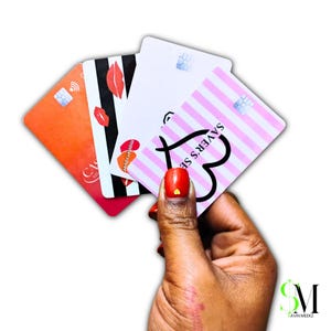 May include: A hand holding a fan of four credit cards. The cards feature various designs, including stripes, lips, and the text "SAVER'S SE". The cards are in shades of orange, red, black, white, and pink.