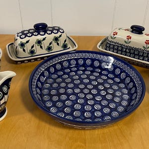 May include: A set of blue and white Polish pottery dishes, including a bowl, a creamer, a butter dish, a serving dish, and a sugar bowl. The dishes feature various floral and swirl patterns.