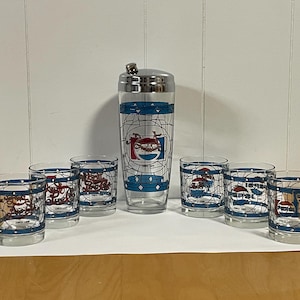 May include: A vintage Pepsi-Cola cocktail set featuring a shaker and six glasses. The glasses and shaker have a blue and white design with the Pepsi logo and the text "Since 1893". The set is displayed on a white surface.