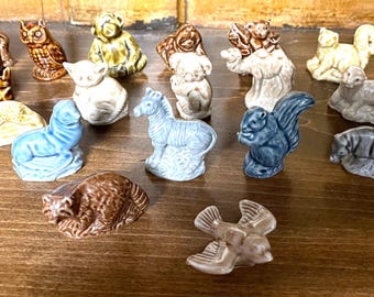 Könnte beinhalten: Eine Sammlung von Keramik-Tierfiguren in verschiedenen Farben, darunter ein Affe, eine Eule, ein Bär, ein Eichhörnchen, ein Zebra und ein Vogel. Die Figuren sind auf einer Holzoberfläche angeordnet und zeigen ihre detaillierten Designs.