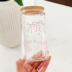May include: A clear glass water bottle with a bamboo lid and a pink bow design. The bottle has a straw.