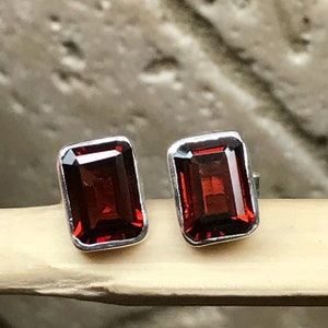 May include: A pair of silver stud earrings with red gemstone accents. The gemstones are rectangular and have a faceted cut.
